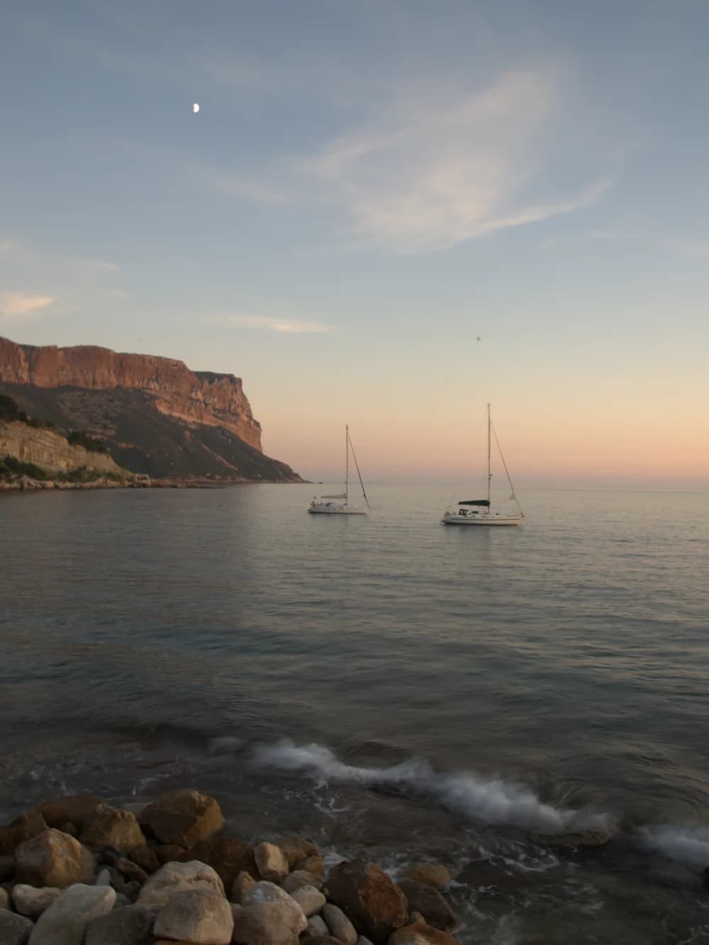 Das Cap Canaille und zwei ankernde Segelboote, in der Dämmerung vom Hafen von Cassis aus gesehen
